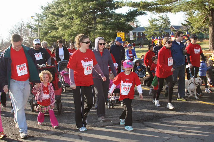 Participants in red race shirts walking and running along a tree-lined neighborhood street